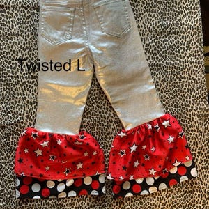 Può includere: Pantaloni metallizzati argentati con un volant a stampa a stelle rosse e bianche e un volant a pois neri e bianchi sul fondo. I pantaloni hanno una cintura e sono etichettati "Twisted L".