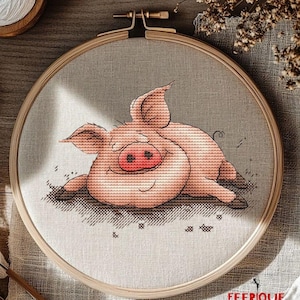 May include: A cross-stitch pattern of a pink pig lying down with its eyes closed. The pig is stitched on a beige fabric and framed in a wooden hoop. The image includes the text "FEERIQUE cross stitch patterns".