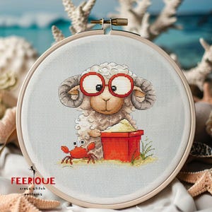 May include: Cross-stitch embroidery in a wooden hoop features a cartoon sheep wearing red glasses, holding a red bucket of sand, and a red crab. The background is a light blue with a beach theme.