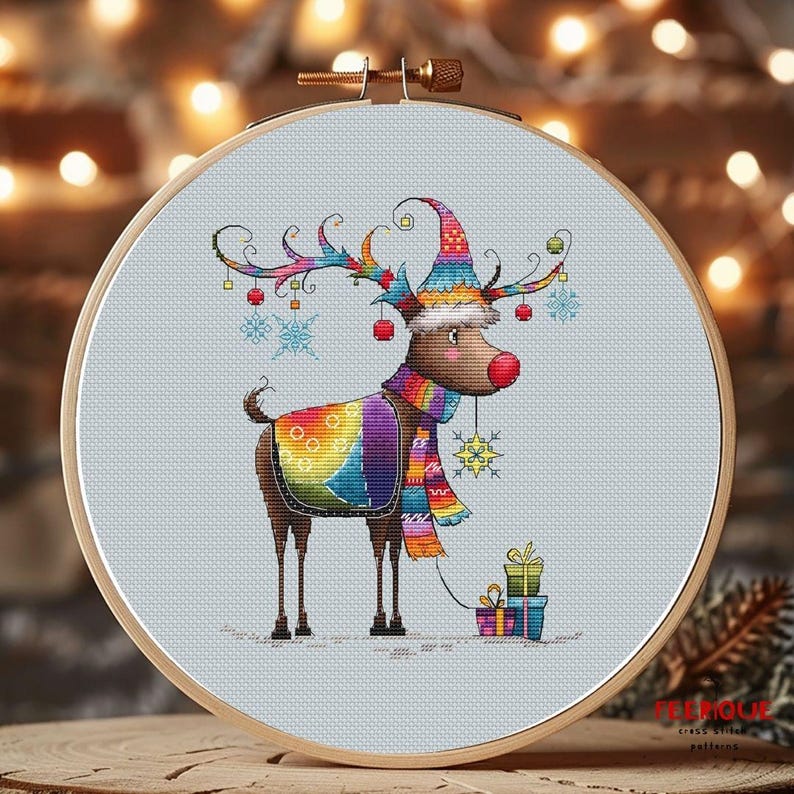 May include: A colorful cross-stitch pattern of a reindeer wearing a festive hat and scarf, holding a gift. The reindeer is surrounded by snowflakes and ornaments.