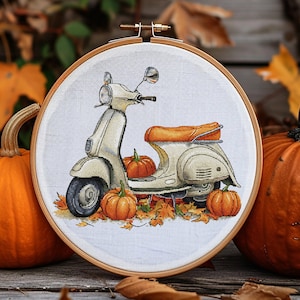 Könnte beinhalten: Kreuzstich-Stickerei in einem Holzrahmen mit einem cremefarbenen Roller mit orangefarbenem Sitz, umgeben von Kürbissen und Herbstblättern. Das Kunstwerk hat ein Herbstthema mit einer rustikalen und saisonalen Ästhetik.