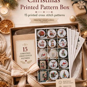 Puede incluir: Una caja de cartón que contiene 15 patrones de punto de cruz impresos con motivos navideños. La caja incluye una etiqueta que dice 15 CHRISTMAS CROSS STITCH PATTERNS y una hoja que muestra varios diseños bordados como osos y renos.