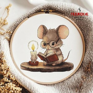 May include: A cross stitch pattern featuring a cute mouse wearing glasses and reading a book by candlelight. The mouse is sitting on a wooden ledge.
