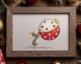 May include: Framed cross-stitch art featuring a cartoon mouse carrying a large Christmas ornament. The ornament is red and white with a dotted pattern. The frame is brown, and the background includes Christmas decorations.