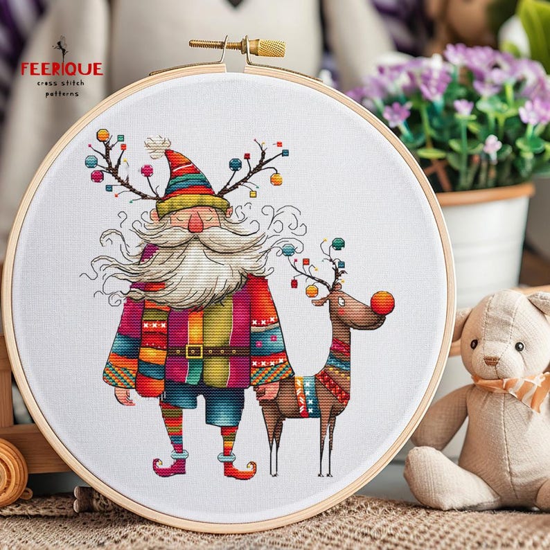 K&ouml;nnte beinhalten: Ein Kreuzstichmuster mit einem farbenfrohen, skurrilen Weihnachtsmann mit langem wei&szlig;em Bart und einem Rentier mit roter Nase. Das Muster ist in einem Holzreifen gerahmt.