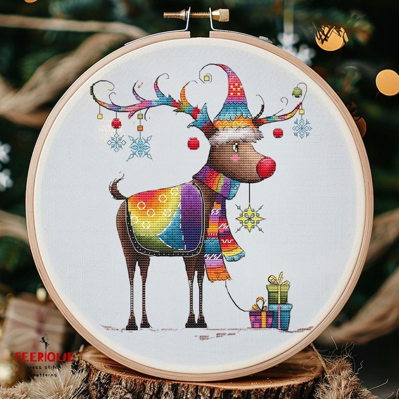 May include: A colorful cross-stitch pattern of a reindeer wearing a rainbow-colored scarf and hat, holding a stack of presents. The reindeer has a red nose and is surrounded by snowflakes.