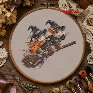 Könnte beinhalten: Ein runder Holzstickrahmen mit einem Kreuzstichmuster von zwei Mäusen, die Hexenhüte und Umhänge tragen und auf einem Besenstiel fliegen. Der Text FEERIQUE cross stitch patterns ist in der oberen rechten Ecke in Rot und Schwarz gedruckt.