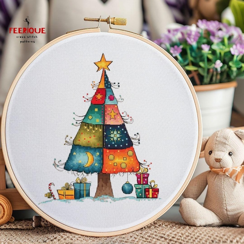 May include: A cross stitch pattern of a colorful patchwork Christmas tree with presents and candy canes. The pattern is displayed in a wooden embroidery hoop.