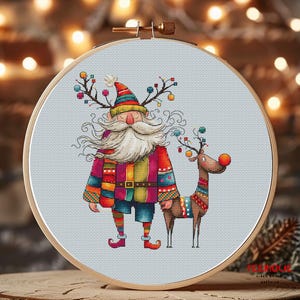 K&ouml;nnte beinhalten: Kreuzstichmuster mit einem farbenfrohen, skurrilen Weihnachtsmann mit langem wei&szlig;em Bart und einem Rentier mit roter Nase. Der Weihnachtsmann tr&auml;gt einen rot-gr&uuml;n-gelb gemusterten Mantel und einen gr&uuml;nen Hut. Das Rentier tr&auml;gt ein buntes, gemustertes Geschirr.