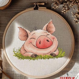 May include: Cross stitch pattern of a smiling pink pig sitting on green grass. The pig has a pink snout and closed eyes. The pattern is framed in a wooden embroidery hoop.
