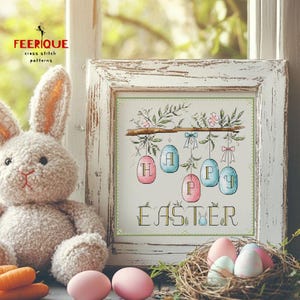 May include: A white wooden frame with a cross-stitch design of colorful Easter eggs spelling out "Happy Easter".