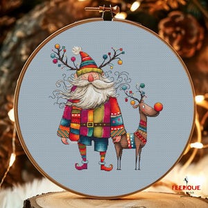 K&ouml;nnte beinhalten: Ein farbenfrohes Kreuzstichmuster mit einem skurrilen Weihnachtsmann mit langem wei&szlig;em Bart und einem Rentier mit roter Nase. Der Weihnachtsmann tr&auml;gt einen bunten gestreiften Pullover und Hut, und das Rentier tr&auml;gt einen bunten gestreiften Pullover. Das Muster ist auf einem hellblauen Hintergrund.