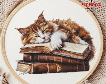 May include: Cross-stitch embroidery of a sleeping cat with brown and white fur atop a stack of old books. The cat is curled up, eyes closed, on the open pages. The embroidery is set in a wooden hoop, with the text "FEERIQUE cross stitch patterns".