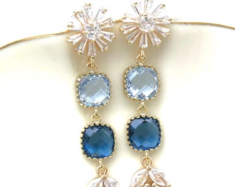May include: Gold dangle earrings with blue and light blue square-shaped gemstones and a crystal flower design at the top.