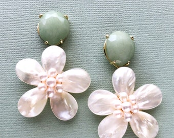 May include: A pair of dangle earrings featuring a white flower design with a pearl center and a green gemstone at the top.