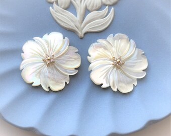 May include: A pair of white mother of pearl flower earrings with gold accents and clear rhinestones in the center of each flower.