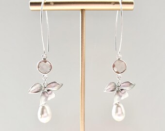 May include: Elegant silver earrings with a floral design. Each earring features a round, smoky quartz stone, a cluster of silver petals, and a dangling pear-shaped pearl. The earrings are displayed on a gold-colored stand.