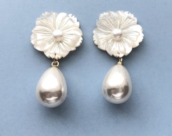 May include: A pair of white pearl drop earrings with a carved flower design. The earrings are made of mother of pearl and feature a large, round pearl drop.