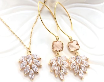 May include: A gold-toned jewelry set consisting of a necklace and a pair of drop earrings. Each piece features a cluster of clear marquise-cut stones arranged in a leaf-like pattern. The earrings include a square-cut peach stone above the leaf design.