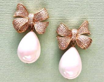 May include: A pair of gold tone earrings with a pearl drop and a bow design. The bows are encrusted with clear rhinestones.