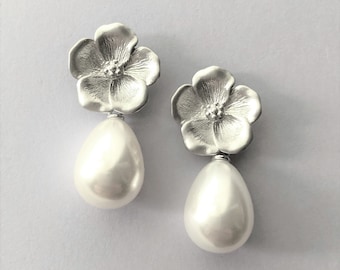 May include: A pair of silver flower earrings with a pearl drop. The flowers are detailed and have a textured finish.