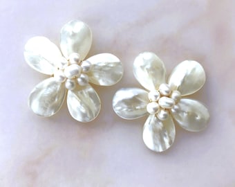May include: A pair of white pearl and shell flower earrings. The earrings are made of white mother of pearl and have a cluster of white pearls in the center.