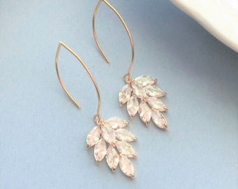 May include: A pair of gold-toned drop earrings with a leaf-like cluster of clear, sparkling crystals. The earrings have a curved hook design and are set against a light blue background.