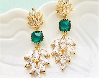 May include: Gold dangle earrings with a green square gemstone and a cluster of clear rhinestones.