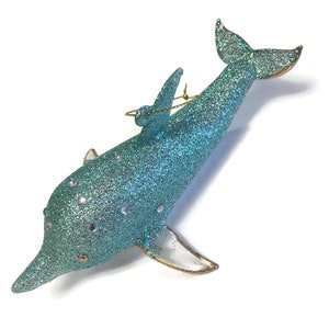 K&ouml;nnte beinhalten: Ein tealblauer Glas-Delfin-Anh&auml;nger mit Glitzer und silbernen Akzenten. Der Delfin hat eine goldene Schnur zum Aufh&auml;ngen.