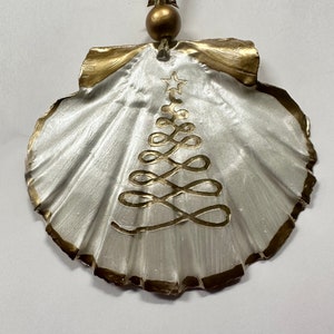 May include: A white seashell ornament with a gold trim and a gold painted Christmas tree design.