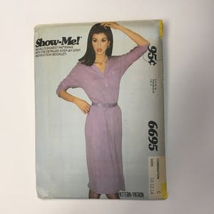 May include: A vintage McCall's Show-Me! sewing pattern for a dress. The pattern is for sizes 10-12-14 and is labeled as combination C. The pattern is 95 cents and features a woman wearing a long-sleeved, light purple dress with a belt.