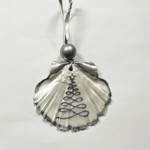 May include: A silver seashell ornament with a silver wire Christmas tree design and a silver bead at the top.