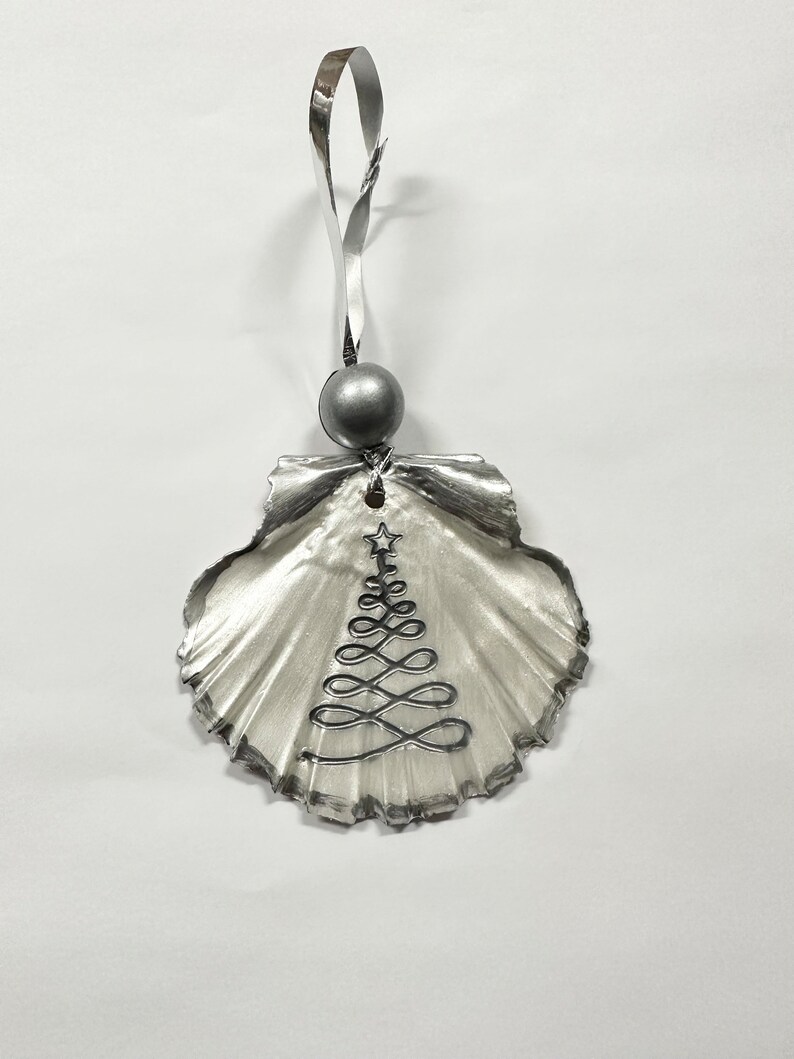 May include: A silver seashell ornament with a silver wire Christmas tree design and a silver bead at the top.