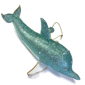 K&ouml;nnte beinhalten: Ein tealblauer Glas-Delfin-Anh&auml;nger mit silbernem Glitzer und einer goldenen Schnur zum Aufh&auml;ngen.