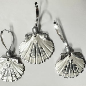 May include: Three silver Christmas ornaments shaped like seashells with a white and gray design of holly leaves and bells.