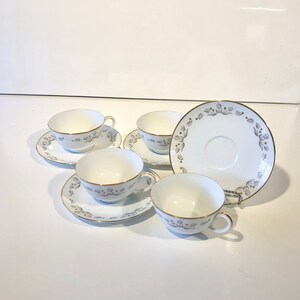 May include: Set of five white teacups and saucers with a delicate floral pattern in gray and gold trim.
