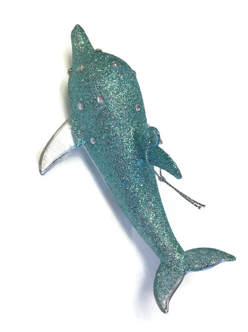K&ouml;nnte beinhalten: Ein tealblauer glitzernder Delfin-Weihnachtsbaumschmuck mit silbernen Akzenten. Der Delfin hat eine silberne Schwanzflosse und eine silberne R&uuml;ckenflosse. Der Anh&auml;nger hat eine silberne Schnur zum Aufh&auml;ngen.