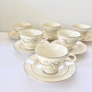 Puede incluir: Juego de seis tazas de té y platillos vintage con un delicado diseño floral en tonos verdes y azules. Las tazas y los platillos son de color blanco cremoso con un borde dorado.