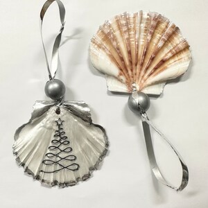 May include: Two silver seashell ornaments with a silver ribbon and bead. One seashell has a silver wire Christmas tree design.