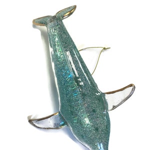 K&ouml;nnte beinhalten: Ein tealblauer Glas-Delfin-Anh&auml;nger mit Glitzer und goldenen Akzenten. Der Delfin hat eine goldene Schnur zum Aufh&auml;ngen.