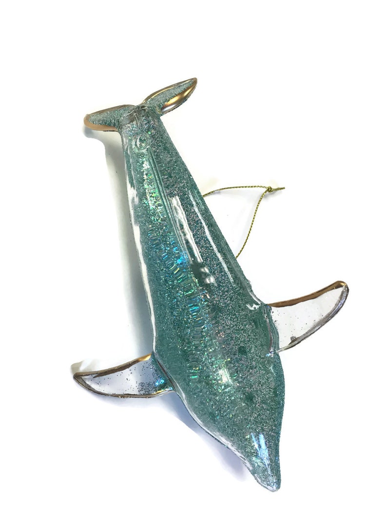 K&ouml;nnte beinhalten: Ein tealblauer Glas-Delfin-Anh&auml;nger mit Glitzer und goldenen Akzenten. Der Delfin hat eine goldene Schnur zum Aufh&auml;ngen.