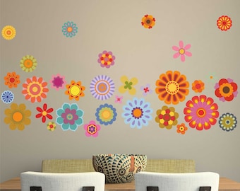 Puede incluir: Un vinilo decorativo de pared con una colección de flores coloridas y estilizadas en varios tamaños y diseños. Las flores son en tonos de naranja, rosa, morado, azul y amarillo, creando una exhibición vibrante y alegre. El vinilo se aplica a una pared de tono neutro.