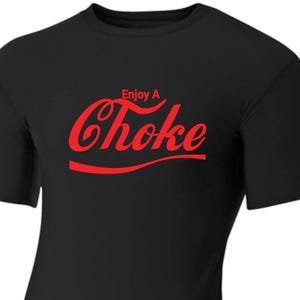 Op de afbeelding: Zwart T-shirt met een rode afbeelding waarop "Enjoy A Choke" staat in een stijl die lijkt op het Coca-Cola-logo.