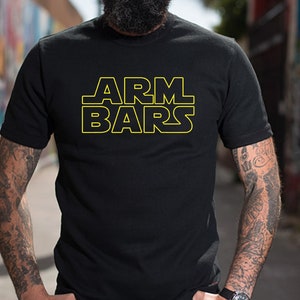Pode incluir: Uma camiseta preta com um gráfico amarelo que diz "ARM BARS" em uma fonte inspirada em Star Wars.