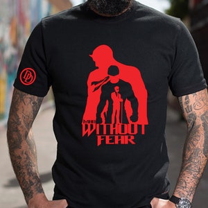 May include: Black t-shirt featuring a red silhouette of Daredevil, the superhero, and the text "MAN WITHOUT FEAR".
