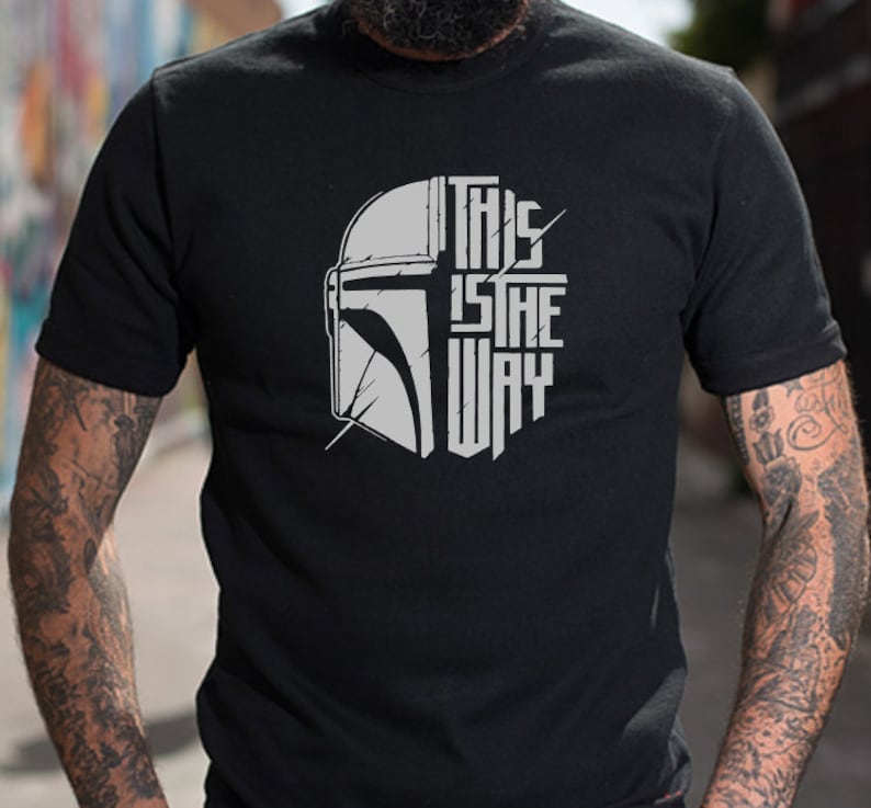 Puede incluir: Camiseta negra con un gr&aacute;fico blanco de un casco mandaloriano y el texto "This is the way".