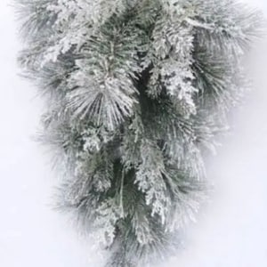 May include: A cascading, artificial pine garland with a frosted, snowy appearance. The garland features long, needle-like leaves in shades of green and is accented with white, creating a wintery aesthetic. The garland is suitable for holiday decor.