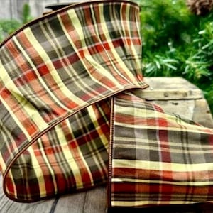 May include: A wide wired ribbon featuring a plaid pattern in shades of dark brown, cream, and burnt orange. The fabric has a structured weave with visible horizontal and vertical lines forming a classic checkered design throughout the material.