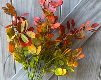 May include: A bouquet of artificial fall foliage with red, orange, and yellow leaves. The leaves are arranged in a cluster and have a realistic appearance.