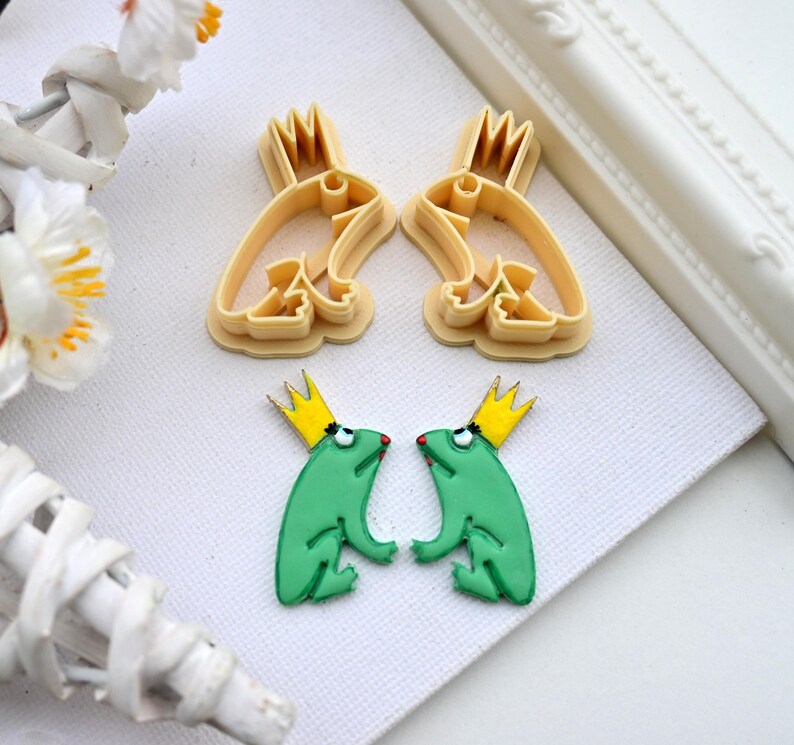 May include: Two green frog cookie cutters with gold crowns and a pair of matching frog cookie cutters in a light brown color.